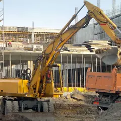 Koparka z uprawnieniami na maszyny budowlane zasypuje ziemią wywrotkę na placu budowy.