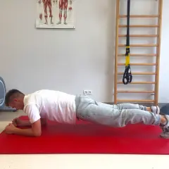 Mężczyzna wykonuje plank, wzmacniając mięśnie core. Obok rower stacjonarny i drabinka gimnastyczna.