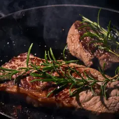 Deux steaks de black angus, poêlés avec du romarin et du gros sel, dégagent une vapeur alléchante.