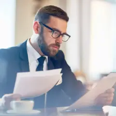 Biznesmen w okularach analizuje dokumenty, zastanawiając się, czy leasing można nadpłacać. Kawa czeka obok.
