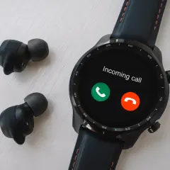 Czarny smartwatch z ekranem pokazującym połączenie przychodzące i bezprzewodowe słuchawki.