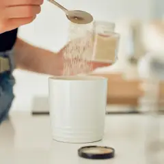 Ręka wsypuje cukier z łyżeczki do białego kubka.