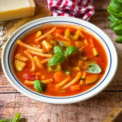 Herzhaftes rezept minestrone original mit viel Gemüse und Pasta, garniert mit frischem Basilikum. Daneben Parmesan und ein Löffel.