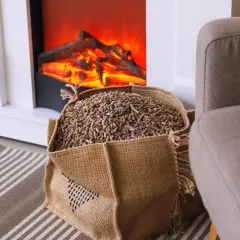 Worek z ekogroszkiem obok sztucznego kominka. Czy ekogroszek to biomasa? Tak, to paliwo odnawialne.