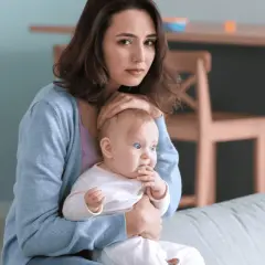 Smutna młoda mama tuli dziecko, czując się przytłoczona. To może być depresja w ciąży, która dotyka wiele kobiet.