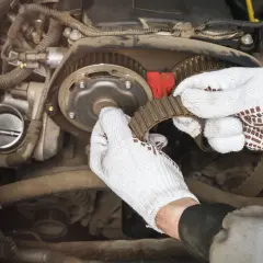Mechanik w białych rękawiczkach wymienia pasek rozrządu. Czas pracy: ile trwa wymiana rozrządu?