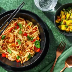 En skål med pad thai med räkor, nudlar, paprika och jordnötter. En liten skål med mangosallad står bredvid.