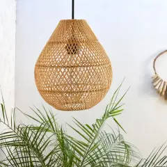 Lámpara colgante de ratán con un diseño de tejido abierto, como un adaptador de pantalla para lámpara, junto a plantas verdes y una decoración de pared de madera.