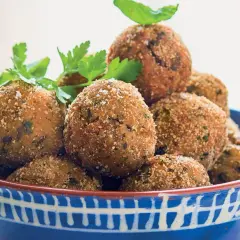 Polpette di melanzane siciliane dorate e croccanti, guarnite con prezzemolo fresco, in una ciotola blu decorata.