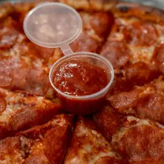Pizza pepperoni z małym kubeczkiem sosu. Czy wolisz keczup czy ketchup?