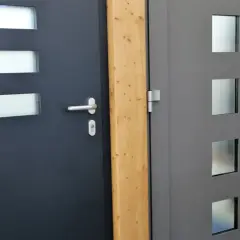 Dwie nowoczesne drzwi wejściowe, jedna ciemnoszara z prostokątnymi przeszkleniami, druga szara z kwadratowymi. Dowiedz się, jak uszczelnić drzwi wejściowe.