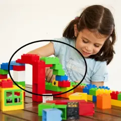 Uśmiechnięta dziewczynka buduje kolorową wieżę z klocków, skupiona na tworzeniu swojej konstrukcji.
