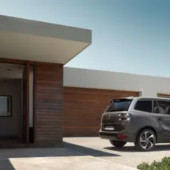 Szary minivan Citroën C4 Picasso zaparkowany przed nowoczesnym domem z drewnianą elewacją.
