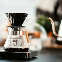 Kaffee tropft in eine Glaskaraffe, während sich der blooming effekt entfaltet. Im Hintergrund eine Kaffeekanne.