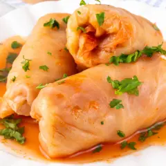 Gołąbki na 1kg mięsa, polane sosem pomidorowym i posypane natką pietruszki, gotowe do podania.