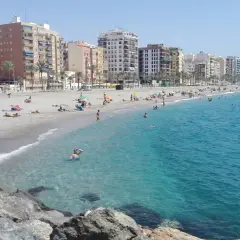 Gente disfrutando del sol y el mar en la playa del Zapillo, con edificios residenciales al fondo.