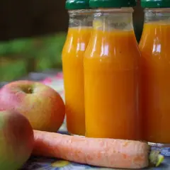 Sok Kubuś na zimę w butelkach, obok jabłka i marchewka.