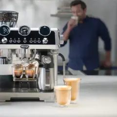 Macchina per caffè De'Longhi in azione, con chicchi pronti per la produzione del caffè. Un uomo assapora una bevanda calda.
