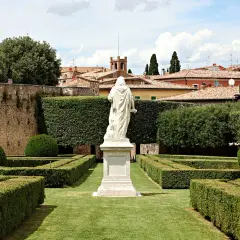 Statua bianca al centro degli Horti Leonini, con siepi geometriche e un muro di pietra.