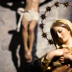 Figurka Matki Bożej z gwiazdami na głowie, w tle ukrzyżowany Jezus. Symbol bólu i cierpienia, jak w różańcu części bolesne.