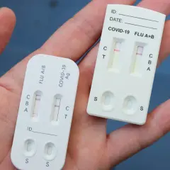 Dłoń trzyma dwa testy combo. Jeden pokazuje pozytywny wynik na grypę, drugi na COVID-19.