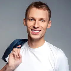 Uśmiechnięty Igor Herbut w białej koszulce z dżinsową kurtką na ramieniu.