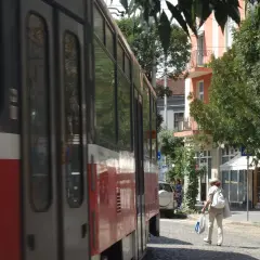 Przejeżdżający tramwaj w słoneczny dzień w Sofii. Kobieta w kapeluszu idzie ulicą z torbami.