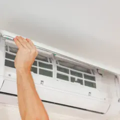 Mains ouvertes pour le nettoyage clim. Les filtres sont visibles à l'intérieur de l'unité murale.
