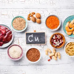 Na tabliczce napisano "Cu". Wokół niej są produkty bogate w miedź: wątróbka, soczewica, fasola, orzechy, krewetki, ryż, kasza gryczana, pszenica, makaron i orzeszki ziemne. Czy miedź rdzewieje? Nie, ale jest niezbędna dla zdrowia.