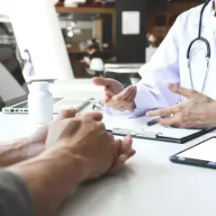 Lekarz wyjaśnia pacjentowi, hcv co to za badanie. Na stole laptop, tablet i leki.