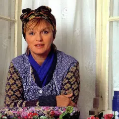 Else Stratmann sitzt am Fenster, eine bunte Kopftuch ziert ihr Haar. Sie trägt eine blaue Bluse mit weißen Punkten und eine Strickjacke.