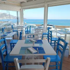 Tavoli apparecchiati con vista mare, perfetti per un apericena a Giardini Naxos. Sedie bianche e blu, un'atmosfera rilassante.