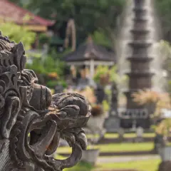 Eine detaillierte Steinskulptur eines Fabelwesens im Vordergrund, im Hintergrund ein Garten mit Brunnen und Pflanzen.