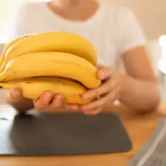 Dłoń trzymająca kiść żółtych bananów na drewnianym stole.
