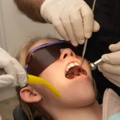 Usta pacjentki otwarte, w nich aparat ortodontyczny. Dentysta używa wiertła i lusterka. Wygląda jakby przygotowywał się do zabiegu, a nie jakby oglądał zwierzęta z rodziny **hyrax**.