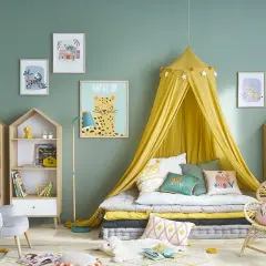 Chambre de fille tendance avec lit au sol, ciel de lit jaune, coussins animaux et étagères en forme de maison.