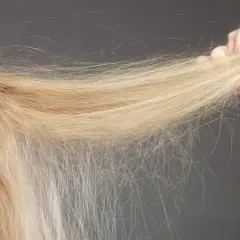 En hand håller en träkam genom blont hår som flyger åt alla håll på grund av statiskt hår.