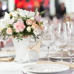 Eleganckie zestawy dań weselnych na białym obrusie, ozdobione bukietem różowych i białych kwiatów.