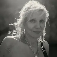 Courtney Love, ikona grunge, z rozwianymi włosami i tatuażem na ramieniu, emanuje siłą.