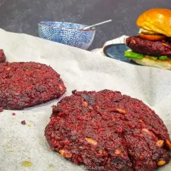 Gotowe burgery z buraka na papierze do pieczenia, jeden złożony burger z bułką i dodatkami w tle.