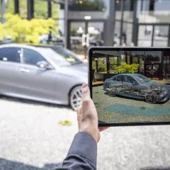 Persona usa una tablet para ver un modelo 3D de un Mercedes, mostrando los componentes internos para entender los mantenimientos.
