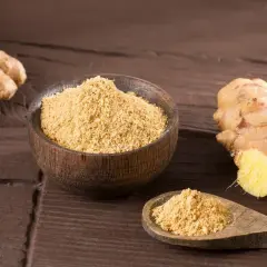 Ingwerpulver verwendung: frischer Ingwer und eine Schale mit feinem Ingwerpulver auf dunklem Holz.