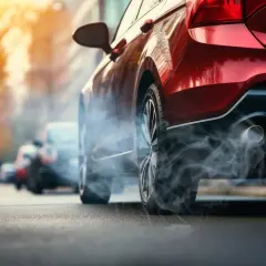 Czerwony samochód stoi na ulicy, z rury wydechowej wydobywa się dym. Zastanawiasz się, ile pali auto na postoju?