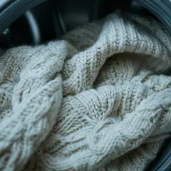 Beżowy, gruby, wełniany sweter warkoczowy w bębnie suszarki. Czy wełniany sweter można suszyć w suszarce? Lepiej nie ryzykować.