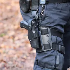 Na udzie funkcjonariusza widoczny jest kabura z pistoletem, co sugeruje, że przemieszczaniem broni jest jego obowiązek.