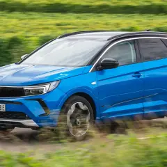 Blå Opel Grandland kör på en landsväg, omgiven av suddiga gröna fält. Kanske ett opel grandland problem med att hålla sig på vägen?