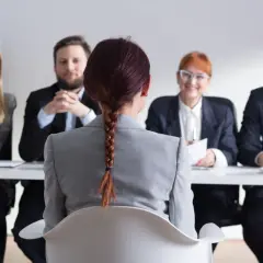 Kobieta warkoczem siedzi przed komisją podczas rozmowy kwalifikacyjnej. Wszyscy uśmiechają się.