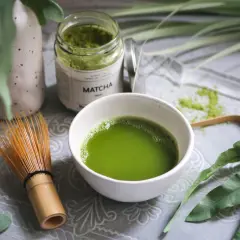 Matcha-Pulver in einem Glas, eine Schale mit zubereitetem Matcha und ein Bambusbesen. Die Matcha-Wirkung auf den Darm wird oft positiv beschrieben.