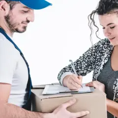 Kurier w niebieskim uniformie podaje paczkę kobiecie, która podpisuje dokumenty.