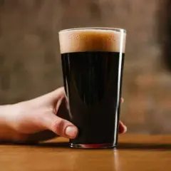 Ręka trzymająca szklankę ciemnego piwa porter. Czy piwo porter jest zdrowe? To pytanie zadaje sobie wielu miłośników tego trunku.
